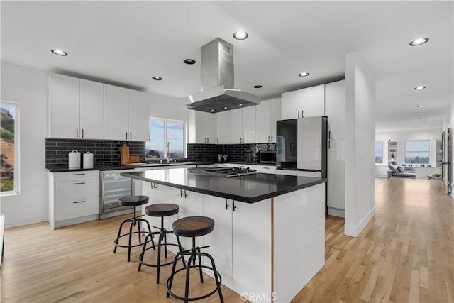 kitchen with wine cooler, island exhaust hood, a healthy amount of sunlight, appliances with stainless steel finishes, and white cabinets