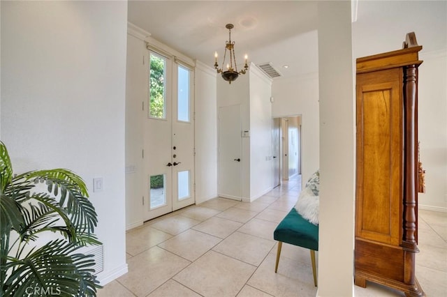 foyer with light tile patterned floors, a chandelier, ornamental molding, and french doors