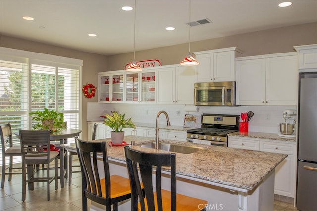 kitchen with a kitchen island with sink, hanging light fixtures, stainless steel appliances, sink, and white cabinets