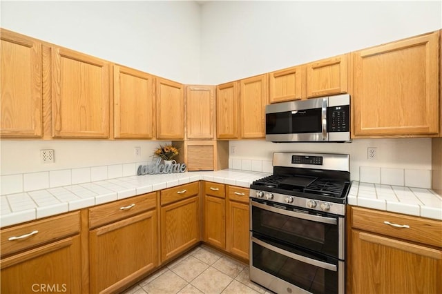 kitchen featuring appliances with stainless steel finishes, a towering ceiling, tile countertops, and light tile patterned floors