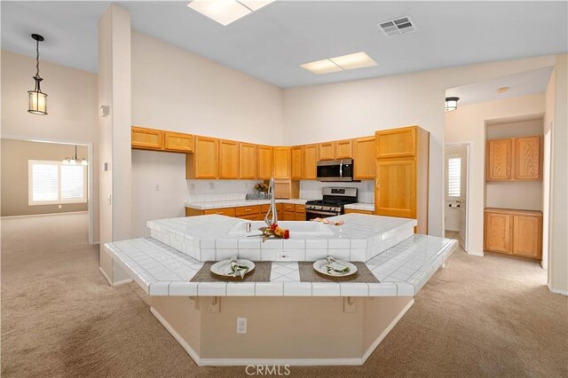 kitchen featuring high vaulted ceiling, tile countertops, light colored carpet, a kitchen bar, and appliances with stainless steel finishes