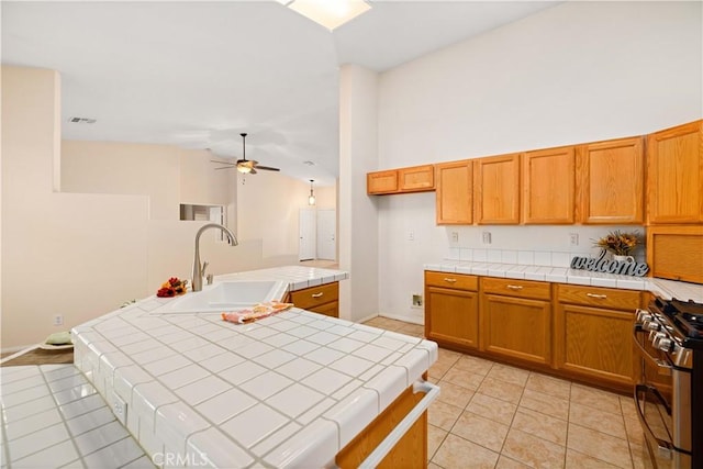 kitchen with gas range, light tile patterned floors, tile counters, and ceiling fan