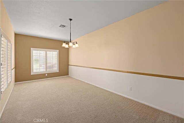 carpeted spare room featuring a chandelier