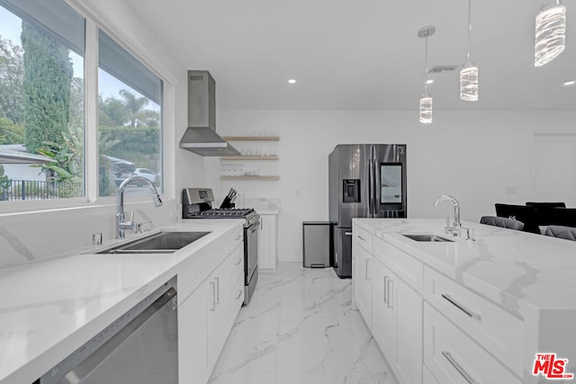 kitchen with wall chimney range hood, sink, white cabinetry, stainless steel appliances, and decorative light fixtures