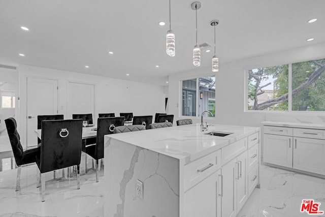 kitchen with light stone countertops, sink, hanging light fixtures, white cabinets, and a center island with sink