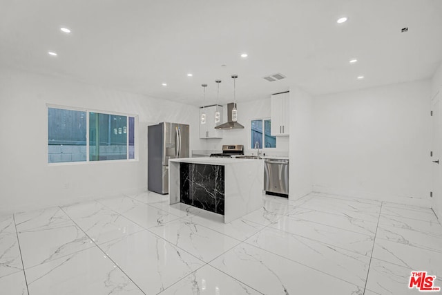 kitchen featuring hanging light fixtures, white cabinetry, stainless steel appliances, wall chimney exhaust hood, and a center island