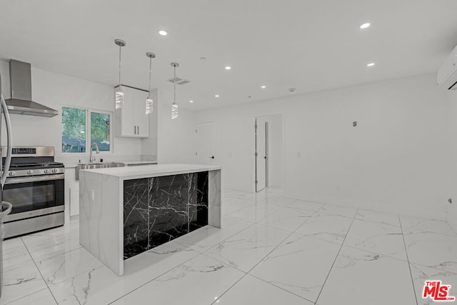 kitchen featuring wall chimney range hood, white cabinets, a kitchen island, stainless steel gas stove, and pendant lighting