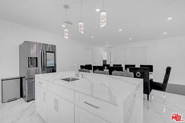 kitchen with sink, stainless steel refrigerator with ice dispenser, white cabinetry, decorative light fixtures, and a kitchen island with sink