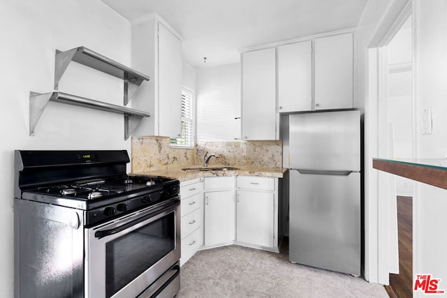 kitchen with tasteful backsplash, appliances with stainless steel finishes, white cabinetry, light stone countertops, and sink