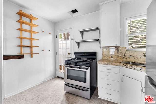 kitchen with backsplash, sink, stainless steel gas range oven, white cabinets, and light stone counters