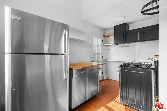 kitchen with black range with gas stovetop, butcher block countertops, backsplash, and stainless steel refrigerator