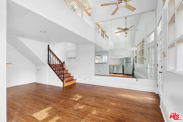 unfurnished living room with a towering ceiling, hardwood / wood-style flooring, and ceiling fan