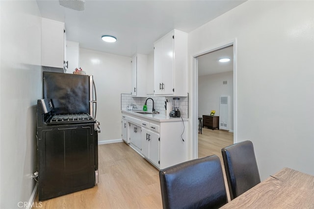 kitchen with white cabinetry, stainless steel refrigerator, sink, and black stove