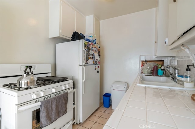 kitchen featuring tile countertops, sink, light tile patterned flooring, white cabinetry, and white appliances