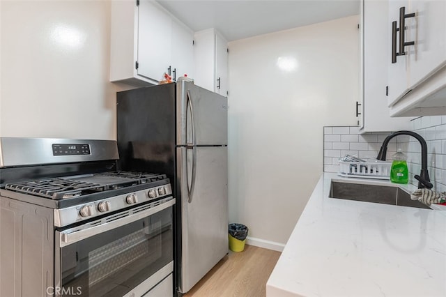 kitchen with tasteful backsplash, white cabinetry, light hardwood / wood-style flooring, sink, and stainless steel appliances