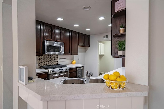 kitchen featuring appliances with stainless steel finishes, sink, dark brown cabinets, kitchen peninsula, and light stone counters