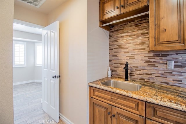 kitchen featuring light hardwood / wood-style flooring, tasteful backsplash, light stone countertops, and sink