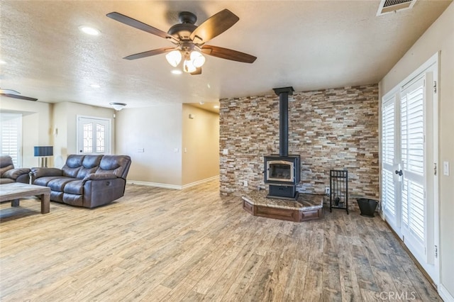 living room with a wood stove, hardwood / wood-style floors, a textured ceiling, and ceiling fan