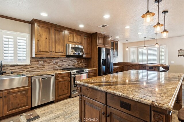 kitchen featuring appliances with stainless steel finishes, sink, a center island, decorative light fixtures, and light hardwood / wood-style flooring