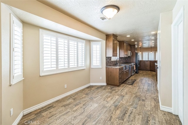 kitchen with black fridge, wood-type flooring, backsplash, light stone countertops, and a textured ceiling