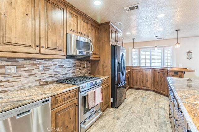 kitchen featuring light stone countertops, appliances with stainless steel finishes, light wood-type flooring, a textured ceiling, and decorative backsplash