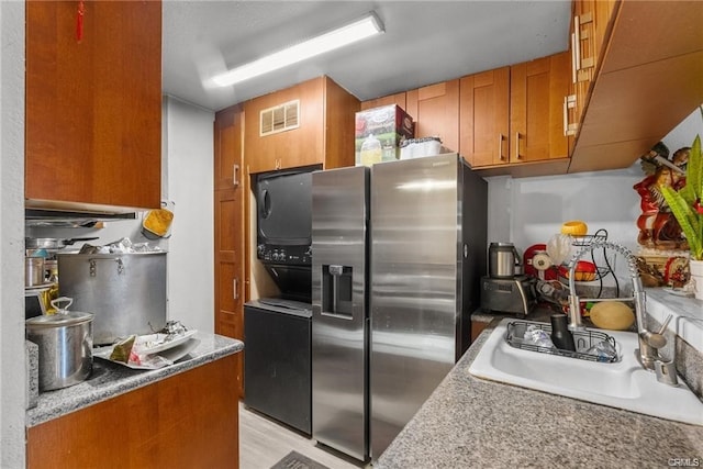 kitchen featuring sink, light wood-type flooring, stainless steel fridge with ice dispenser, and stacked washer and clothes dryer