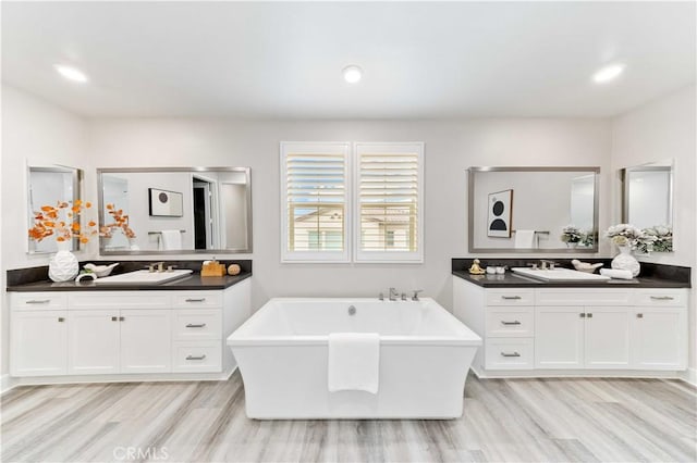 bathroom with a washtub, vanity, and wood-type flooring