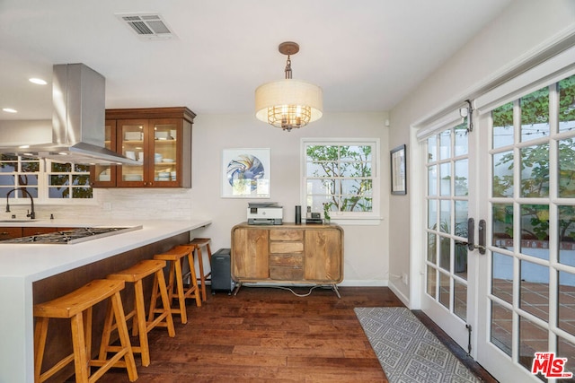 kitchen with island range hood, kitchen peninsula, backsplash, dark wood-type flooring, and stainless steel gas cooktop