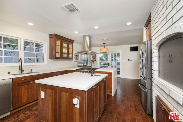 kitchen featuring decorative light fixtures, stainless steel appliances, sink, island range hood, and a center island with sink