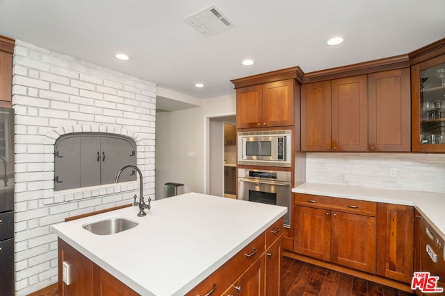 kitchen with appliances with stainless steel finishes, an island with sink, decorative backsplash, sink, and dark hardwood / wood-style floors