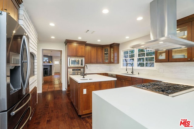 kitchen featuring stainless steel appliances, an island with sink, sink, backsplash, and island range hood