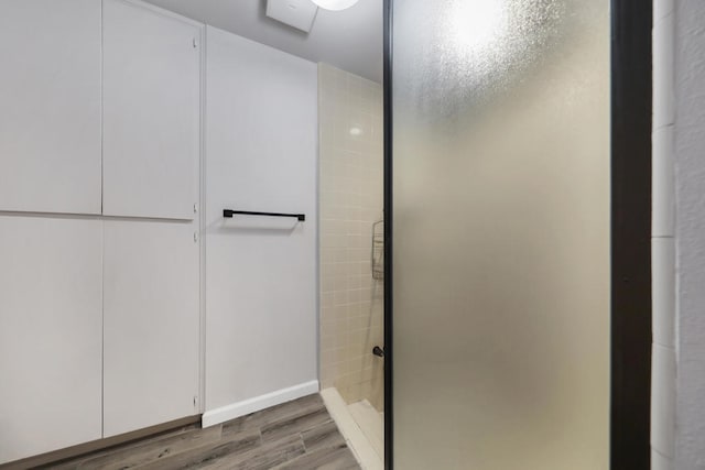 bathroom with a tile shower and wood-type flooring