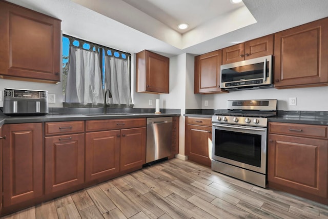 kitchen featuring light hardwood / wood-style flooring, a raised ceiling, appliances with stainless steel finishes, and sink