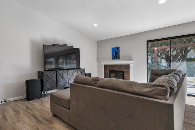 living room featuring lofted ceiling, hardwood / wood-style floors, and a tiled fireplace