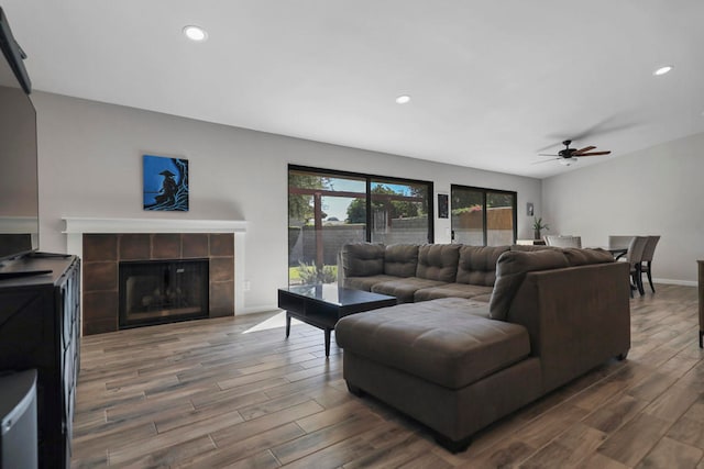 living room with ceiling fan, a tiled fireplace, and dark hardwood / wood-style flooring