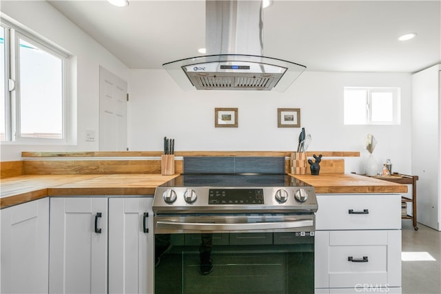 kitchen with butcher block countertops, white cabinets, island range hood, and stainless steel range with electric cooktop