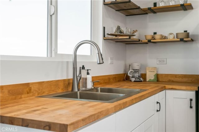 kitchen with butcher block countertops, white cabinetry, and sink