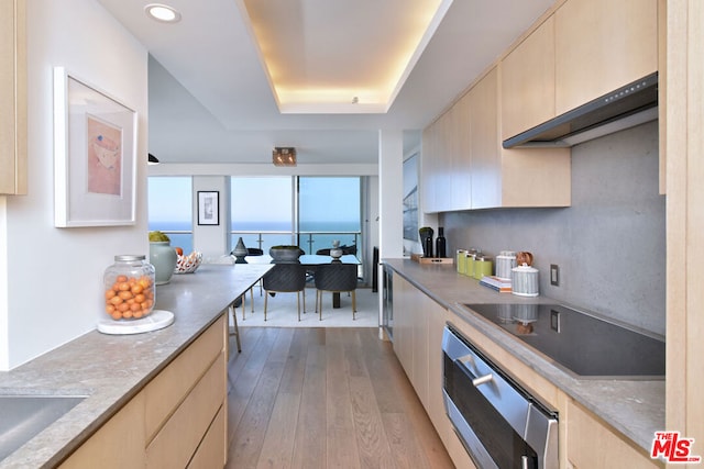 kitchen with oven, light wood-type flooring, light brown cabinetry, a tray ceiling, and stovetop