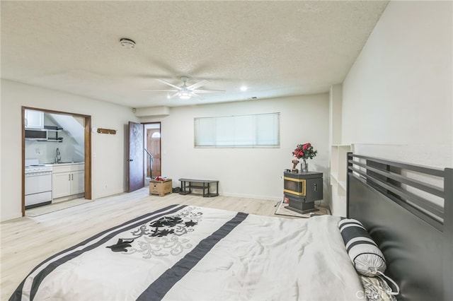 bedroom with light hardwood / wood-style floors, a wood stove, a textured ceiling, and ceiling fan