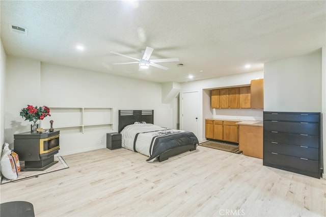 bedroom featuring a textured ceiling, light wood-type flooring, and a wood stove