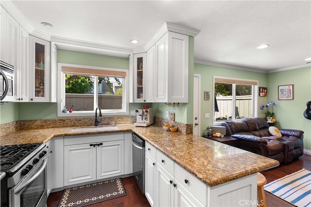 kitchen with kitchen peninsula, sink, white cabinetry, light stone countertops, and appliances with stainless steel finishes