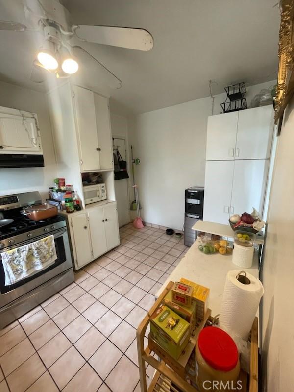 kitchen featuring ceiling fan, exhaust hood, stainless steel stove, white cabinetry, and light tile patterned flooring