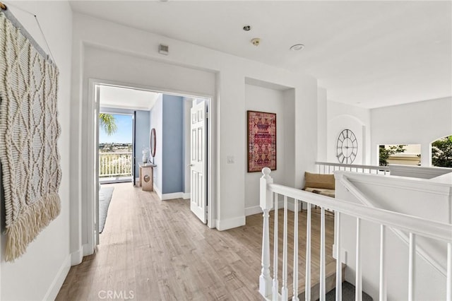 hallway with an upstairs landing, light wood-style floors, and baseboards