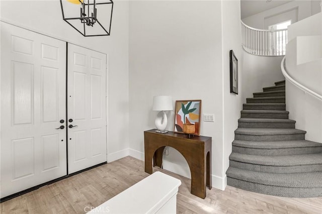 entrance foyer with baseboards, a chandelier, stairway, a towering ceiling, and wood finished floors