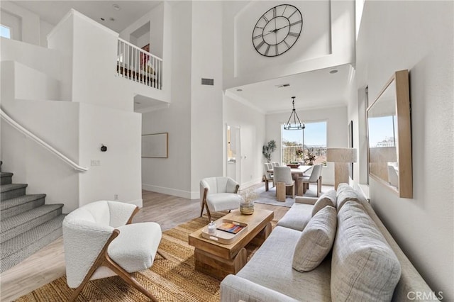 living area with visible vents, a notable chandelier, wood finished floors, a towering ceiling, and stairs