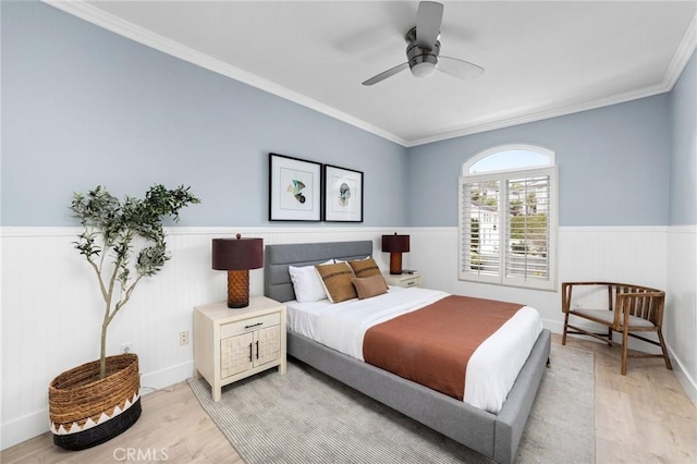 bedroom featuring wainscoting, a ceiling fan, crown molding, and light wood-style floors