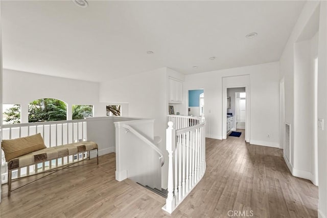 corridor featuring visible vents, an upstairs landing, baseboards, and light wood finished floors