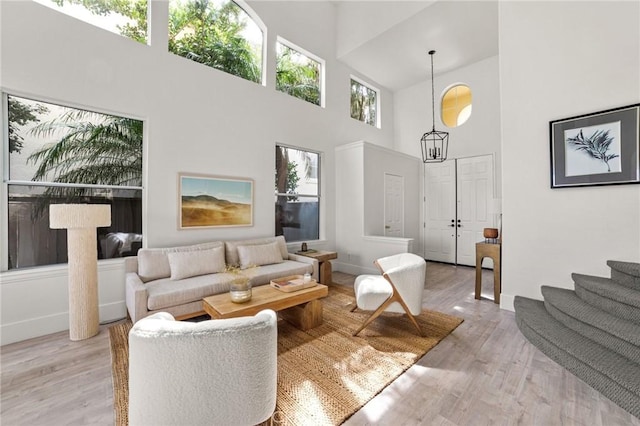 living area with stairs, baseboards, light wood-type flooring, and a towering ceiling