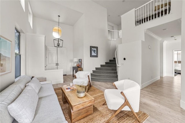 living room with crown molding, baseboards, stairway, light wood-type flooring, and a high ceiling