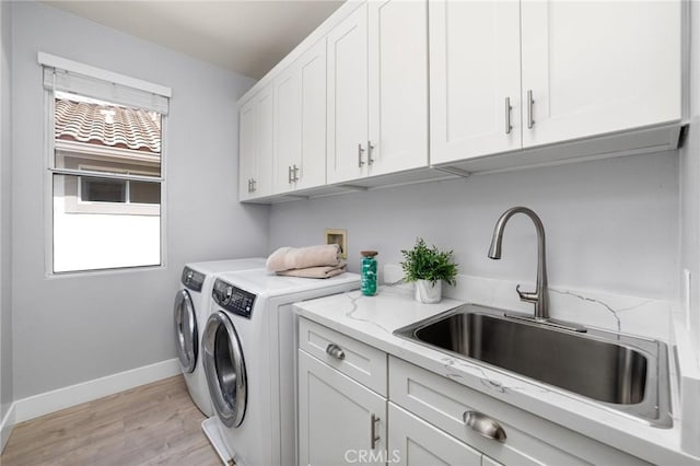 washroom with baseboards, washing machine and dryer, light wood-style floors, cabinet space, and a sink